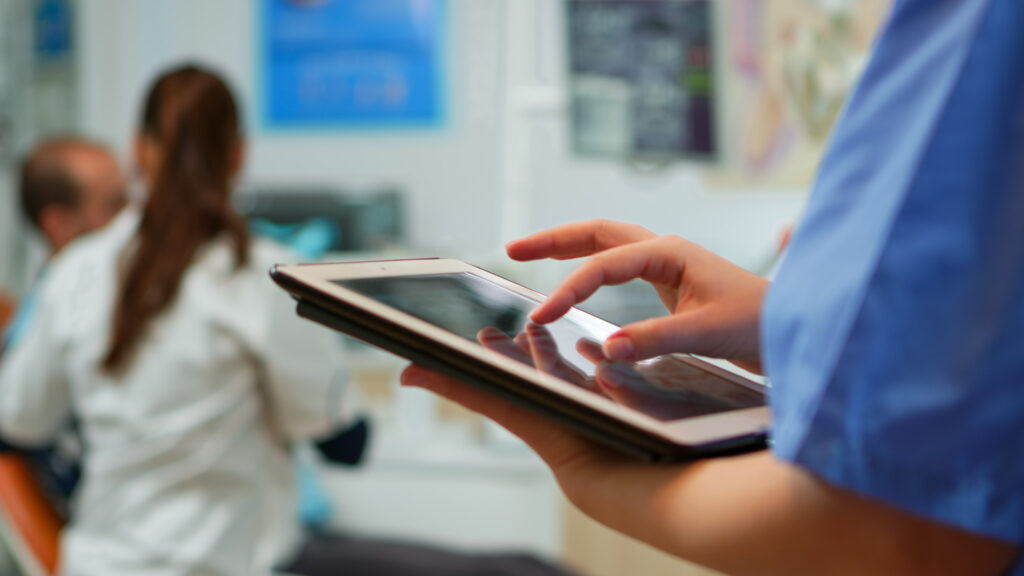 Close up of nurse holding and typing on tablet Close up of nurse holding and typing on tablet standing in stomatologic clinic, while doctor is working with patient in background. Using monitor with chroma key izolated pc key mockup pc display